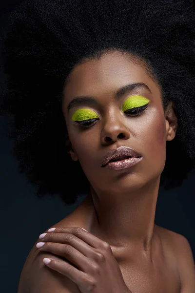 Ritratto di bella modella afroamericana con brillante trucco al neon e spalle nude isolate su nero — Foto stock