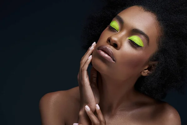 Ritratto di bella modella afroamericana con brillante trucco al neon e spalle nude isolate su nero — Foto stock