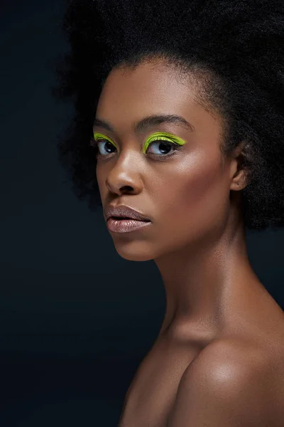 Retrato de hermoso modelo afroamericano con maquillaje de neón brillante y hombros desnudos aislados en negro - foto de stock
