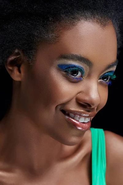 Retrato de sonriente modelo afroamericano con ojos azules brillantes sombras aisladas en negro - foto de stock