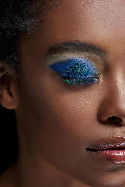Vista parcial de mujer afroamericana con sombra de ojos azul brillante aislada en azul - foto de stock
