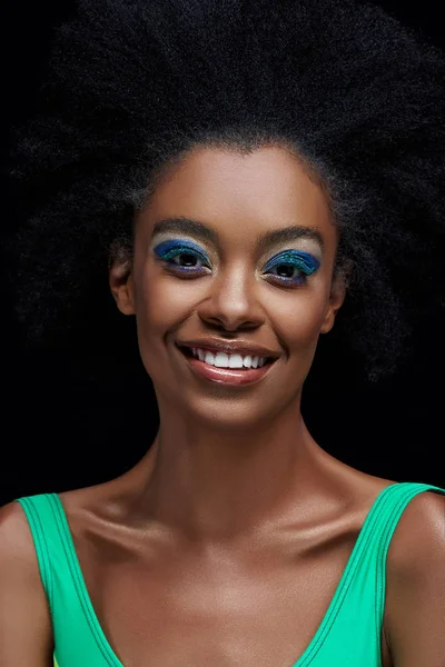 Retrato de sonriente modelo afroamericano con ojos azules brillantes sombras aisladas en negro - foto de stock