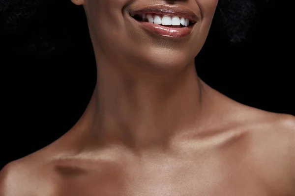 Обрезанный снимок улыбающейся африканской женщины с голыми плечами, изолированными на черном — стоковое фото