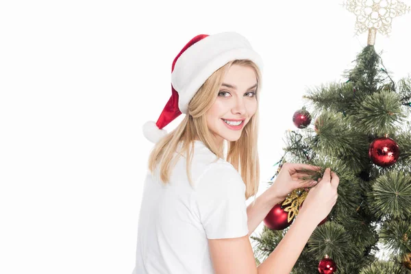 Lächelnde Frau mit Weihnachtsmann-Hut schmückt Weihnachtsbaum isoliert auf Weiß — Stockfoto