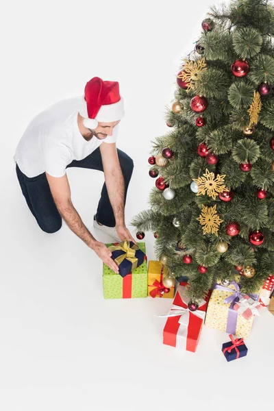 High angle view of man in santa claus hat putting gift under christmas tree isolated on white — Stock Photo