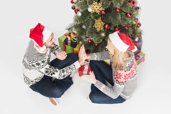 High angle view of couple in sweaters and santa claus hats playing patty cake game near christmas tree isolated on white — Stock Photo