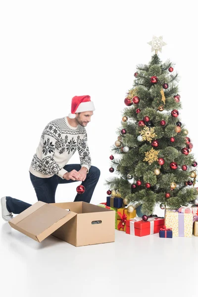 Man in sweater ad santa claus hat decorating christmas tree alone isolated on white — Stock Photo