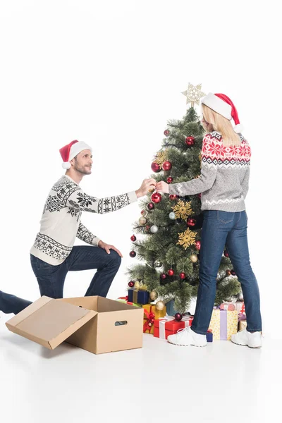 Дівчина і хлопець у капелюхах Санта Клауса, які прикрашають ялинку разом ізольовані на білому — стокове фото