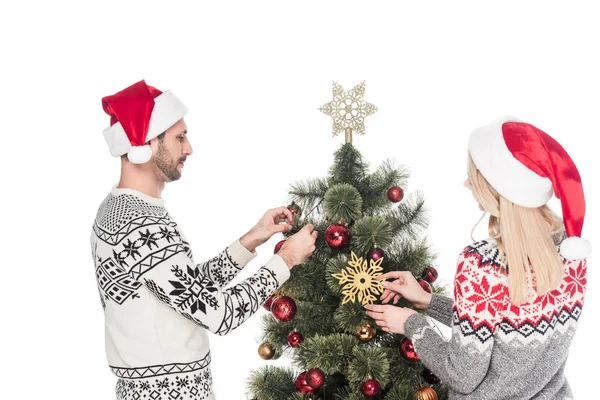 Novia y novio en suéteres y sombreros de Santa Claus decorando árbol de Navidad juntos aislados en blanco - foto de stock