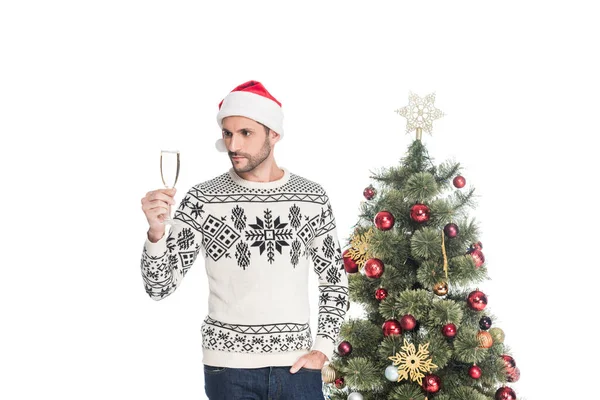 Hombre en suéter y sombrero de santa claus con copa de champán de pie cerca del árbol de Navidad aislado en blanco — Stock Photo