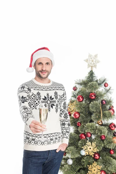 Portrait of man in sweater and santa claus hat with glass of champagne standing near christmas tree isolated on white — Stock Photo