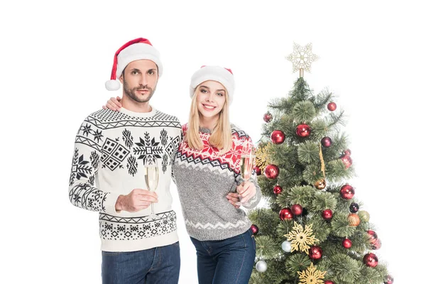 Sorrindo casal apaixonado em chapéus de santa claus com copos de champanhe na árvore de natal isolado em branco — Fotografia de Stock