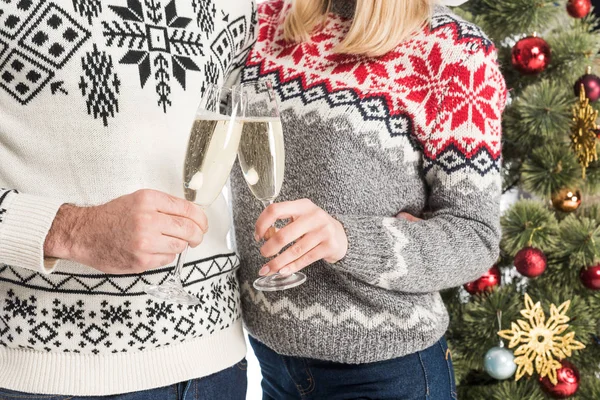 Recortado disparo de pareja en suéteres tintineo vasos de champán aislado en blanco - foto de stock