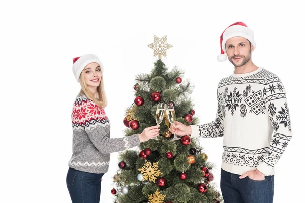 Vista lateral de pareja sonriente en amor tintineo copas de champán en el árbol de Navidad aislado en blanco - foto de stock