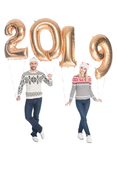 Coppia elegante in maglioni e cappelli di Babbo Natale con palloncini 2019 isolati su bianco, concetto di nuovo anno 2019 — Foto stock