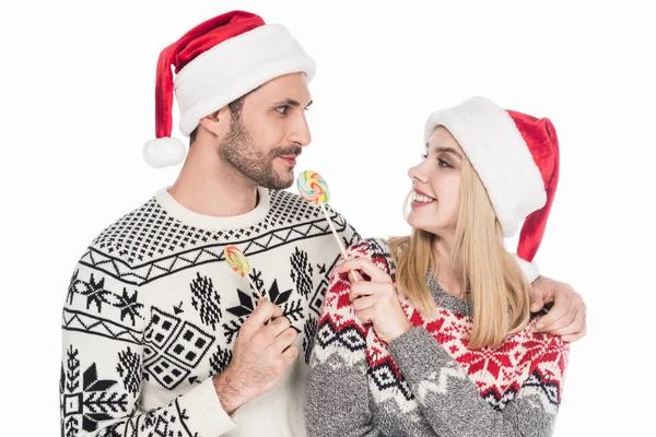 Porträt eines kaukasischen Paares in Weihnachtsmannhüten mit Lutschern auf weißem Grund — Stockfoto