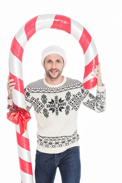 Retrato de hombre joven en suéter y sombrero de santa claus con caramelo de juguete aislado en blanco — Stock Photo