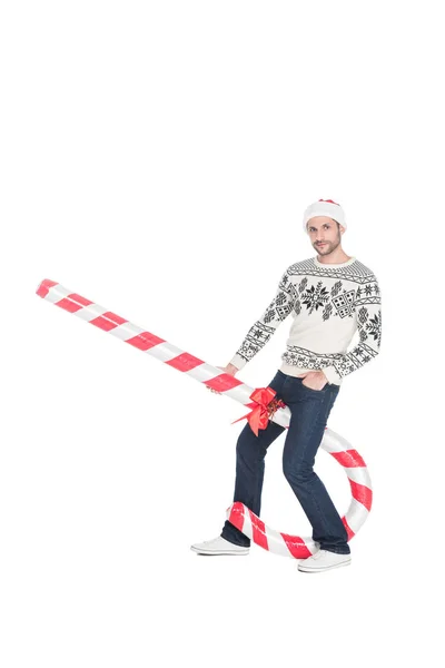 Hombre joven en suéter y sombrero de santa claus con caramelo de juguete aislado en blanco — Stock Photo