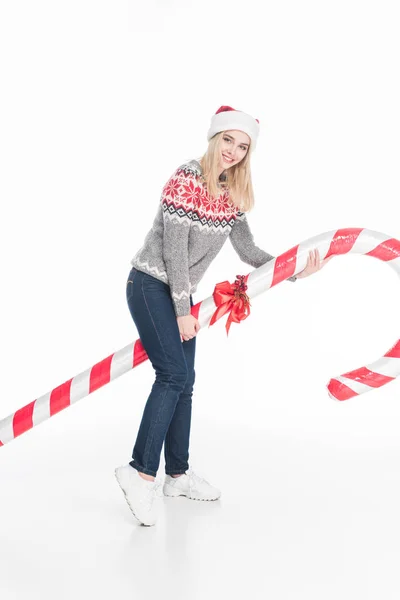 Young woman in sweater and santa claus hat holding toy candy isolated on white — Stock Photo