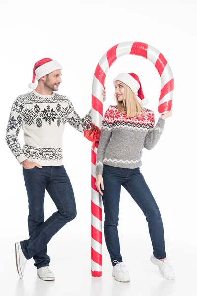 Junges Paar in Weihnachtsmannmützen und Pullovern mit Spielzeugbonbons auf weißem Hintergrund — Stockfoto