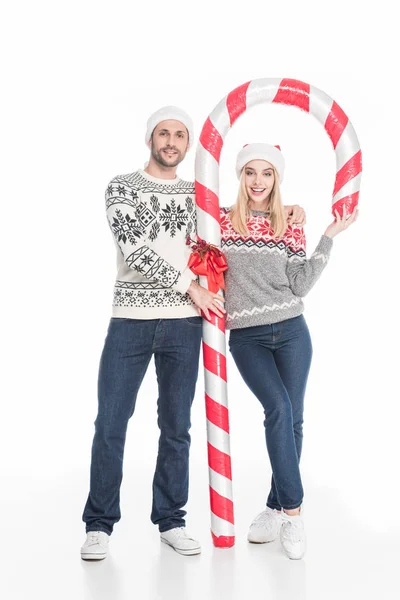 Sonriente pareja en santa claus sombreros y suéteres con juguete caramelo aislado en blanco — Stock Photo