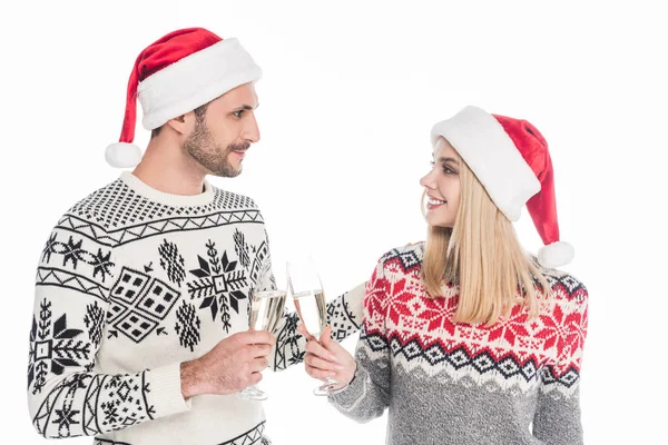Casal em camisolas e chapéus de Papai Noel clinking copos de champanhe isolado em branco — Fotografia de Stock