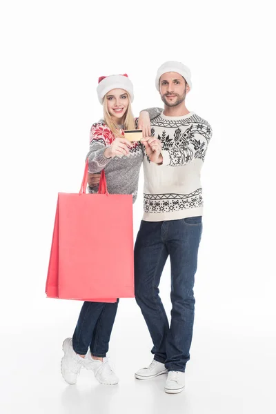 Paar in Weihnachtsmannmützen mit Einkaufstaschen und Kreditkarte isoliert auf weiß — Stockfoto