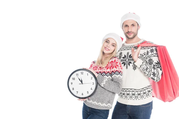 Retrato de pareja joven en sombreros de Santa Claus con reloj y bolsas aisladas en blanco - foto de stock