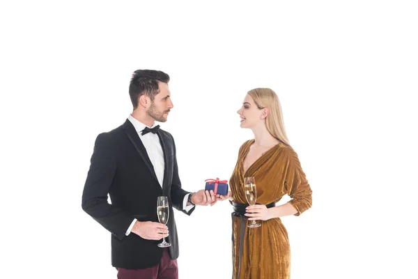 Stilvoller Mann überreicht Geschenk an lächelnde Freundin mit Glas Champagner isoliert auf Weiß — Stockfoto