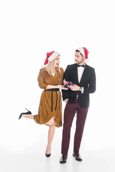 Élégant jeune couple dans chapeaux santa claus avec cadeau de Noël enveloppé isolé sur blanc — Photo de stock