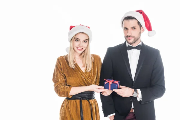 Retrato de pareja joven con estilo en sombreros de Santa Claus con regalo de Navidad envuelto aislado en blanco - foto de stock
