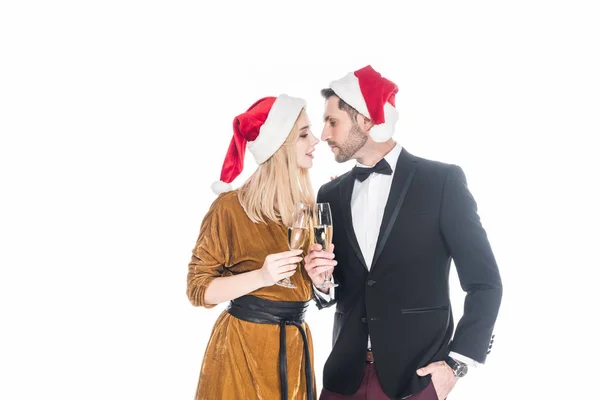 Portrait of stylish couple in santa claus hats clinking glasses of champagne isolated on white — Stock Photo