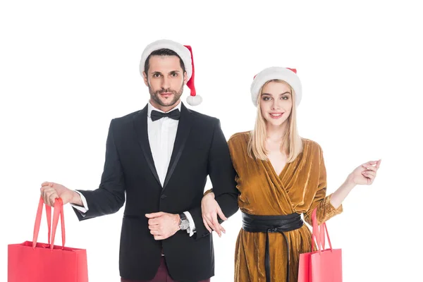Ritratto di coppia attraente in cappelli di Babbo Natale con borse della spesa isolate su bianco — Foto stock