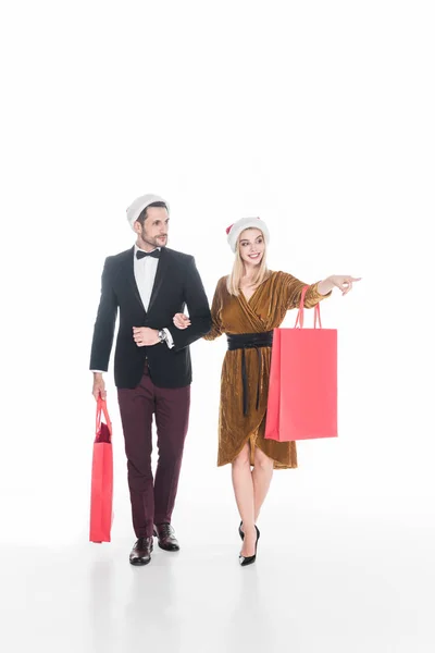 Attraktives Paar in Weihnachtsmannmützen mit Einkaufstaschen auf weißem Grund — Stockfoto