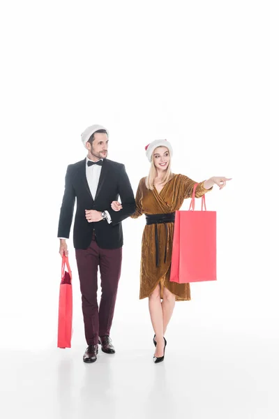 Beau couple dans chapeaux santa claus avec des sacs à provisions isolés sur blanc — Photo de stock