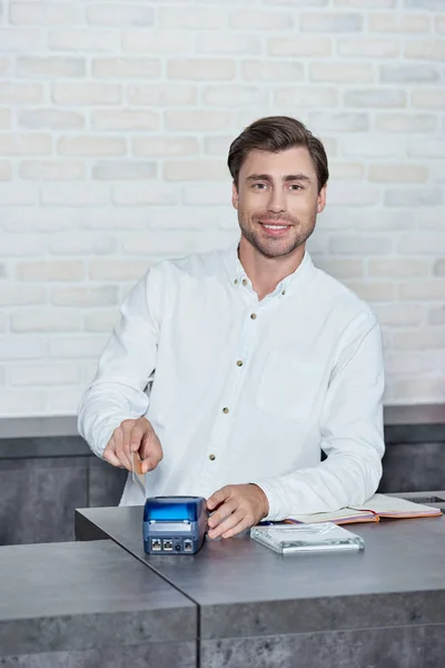 Jeune vendeur souriant tenant une carte de crédit et utilisant le terminal de paiement dans la boutique — Photo de stock