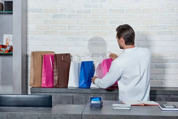 Vista trasera del joven que trabaja con bolsas de compras en la tienda - foto de stock