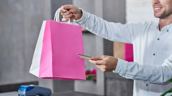 Recortado disparo de vendedor sonriente sosteniendo bolsas de compras y tarjeta de crédito en la tienda - foto de stock