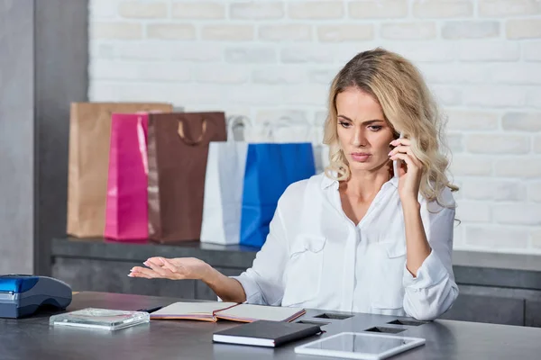 Емоційна молода жінка розмовляє по смартфону під час роботи в магазині — стокове фото