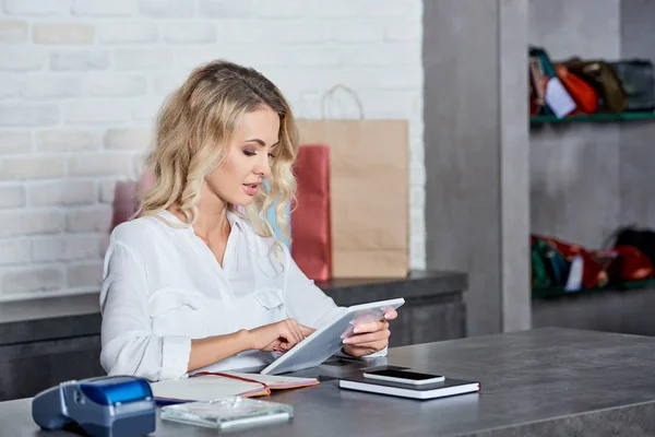 Hermosa mujer joven usando tableta digital mientras trabaja en la tienda — Stock Photo