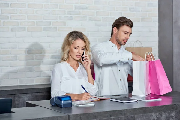 Junge Frau spricht mit Smartphone und Kollegin hält Einkaufstüten im Laden — Stockfoto