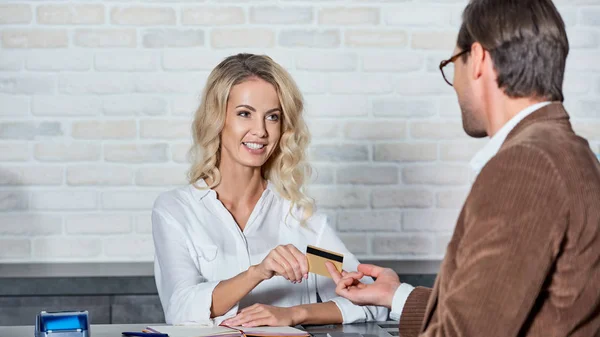 Клієнт надає кредитну картку усміхненому молодому продавцю в магазині — стокове фото