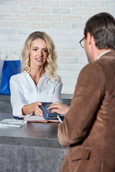 Cropped shot of customer and smiling young seller using payment terminal in shop — Stock Photo