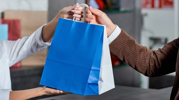 Tiro recortado del vendedor y el comprador que sostiene bolsas de compras en la tienda - foto de stock