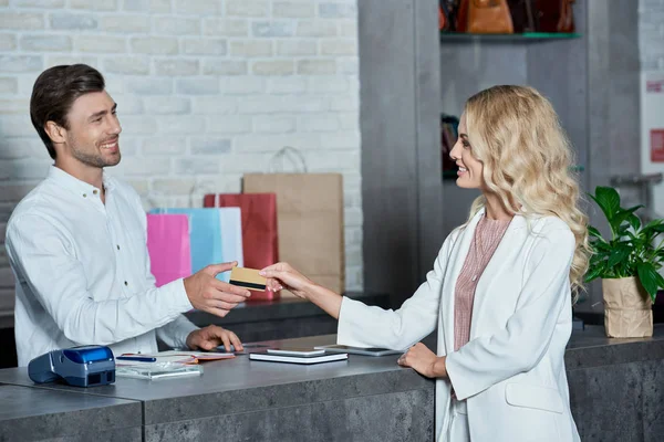 Smiling young customer giving credit card to salesman in shop — Stock Photo