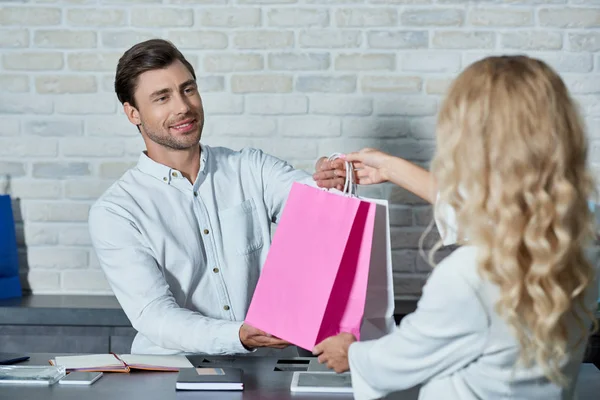 Trabalhador da loja sorridente e jovem cliente do sexo feminino segurando sacos de compras na loja — Fotografia de Stock