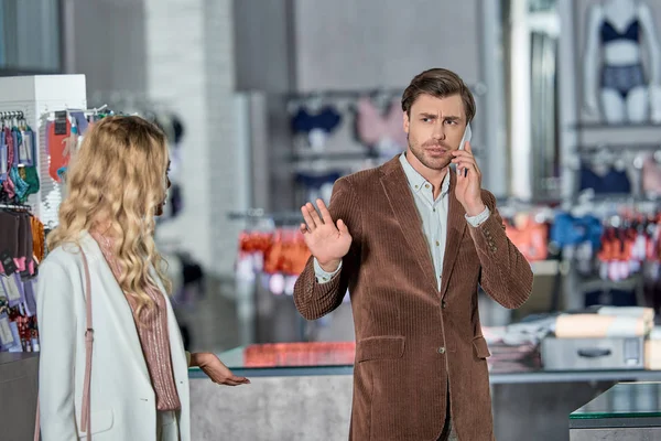 Young man talking by smartphone and gesturing to woman in shop — Stock Photo