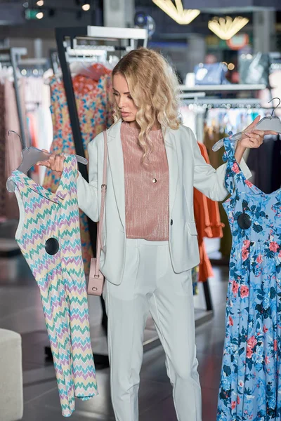Junge Frau hält Kleiderbügel mit stylischen Kleidern beim Einkaufen in Boutique — Stockfoto