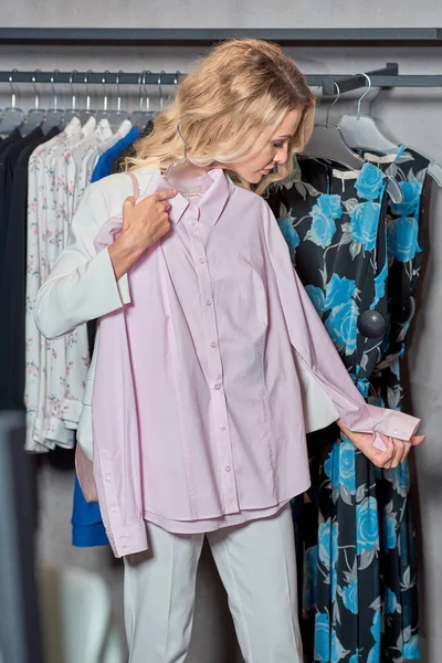 Mulher atraente segurando cabide com camisa elegante na boutique — Fotografia de Stock