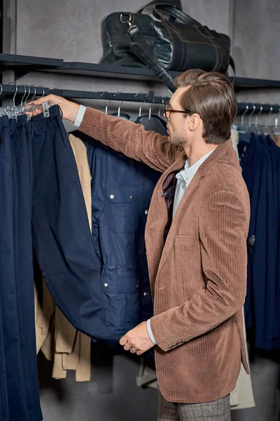 Handsome stylish man in eyeglasses choosing fashionable clothes in shop — Stock Photo